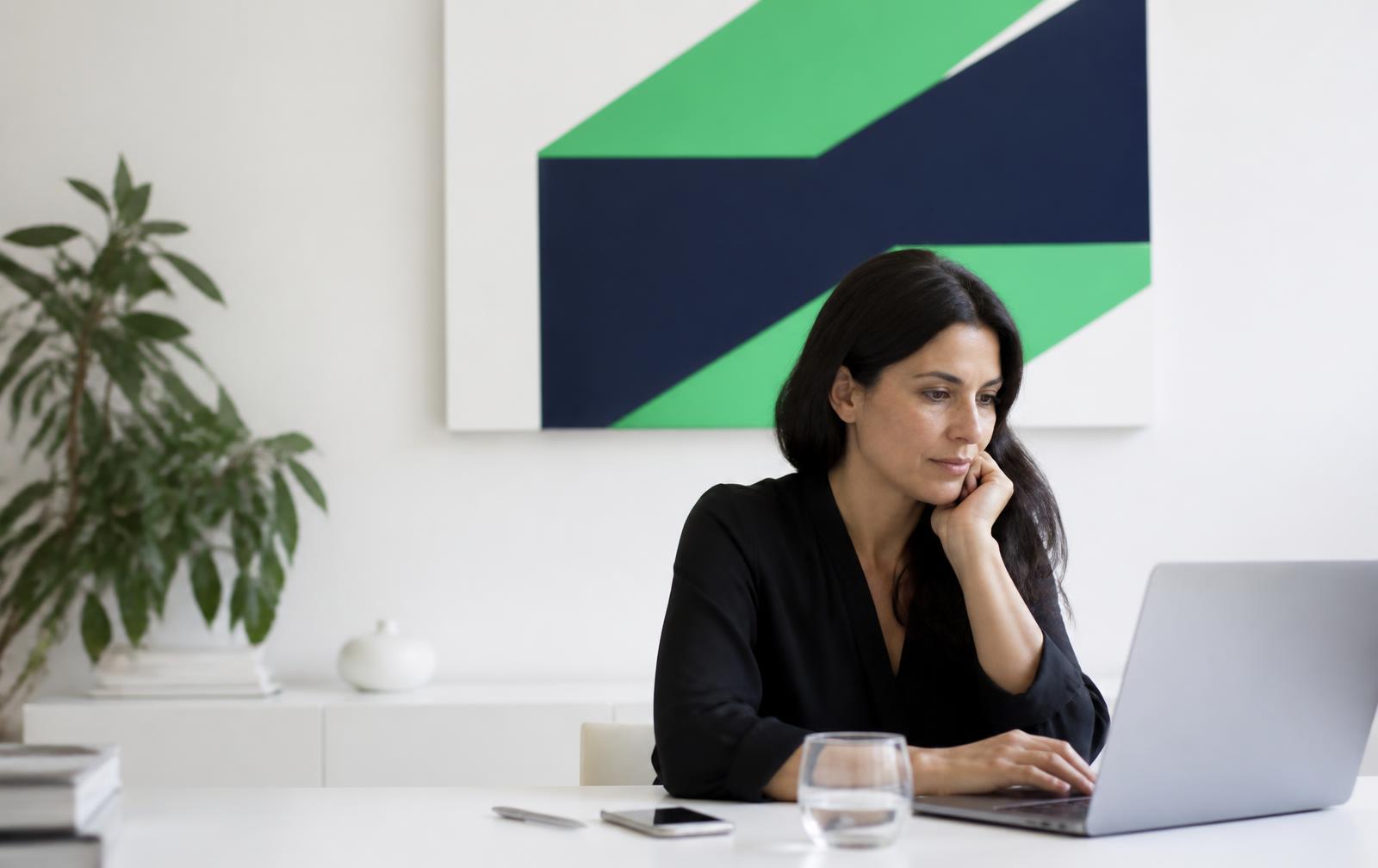 Pessoa sentada a uma mesa branca, a olhar com atenção para o portátil.